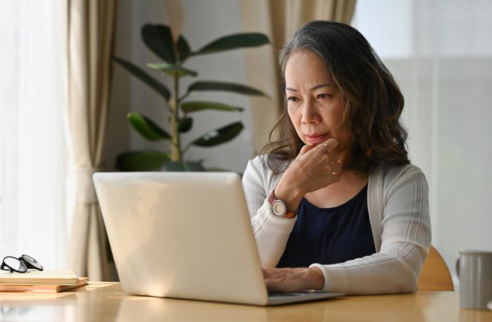 Older Asian woman looking at laptop with contemplative pose